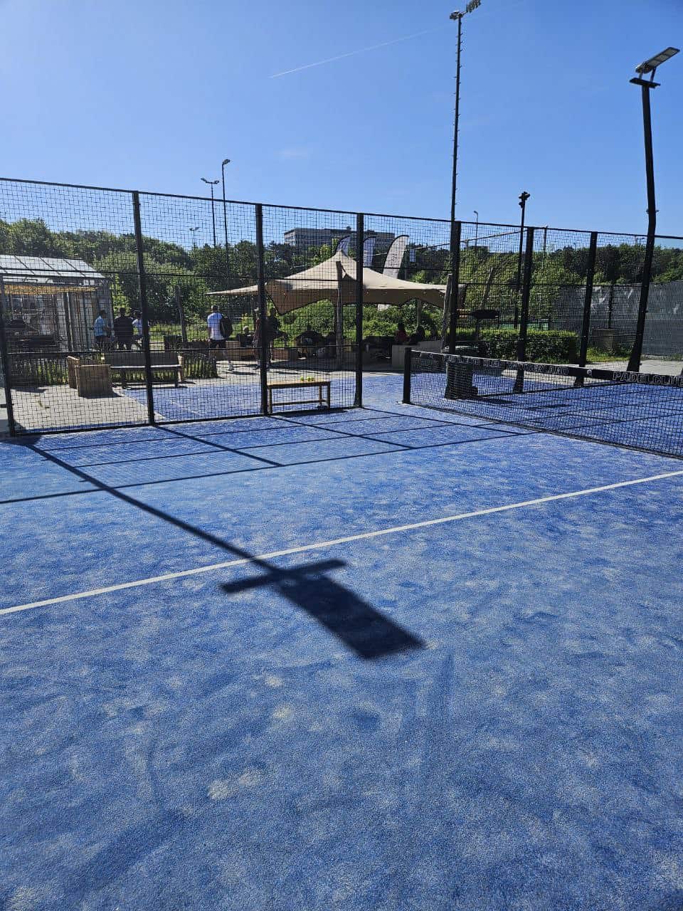 Luchtfoto van een padelbaan bij NXT Level Padelacademy met omringend groen en een heldere blauwe hemel, perfect voor padeltraining en recreatief speelplezier.